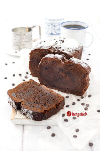 Schokokuchen nach einem Frischkäse-Schokoladenkuchen Rezept von herzelieb. Der Kuchen liegt auf eine weißen Brett und ist angeschnitten. Eine Scheibe lehnt am Kuchenlaib, die andere liegt davor.