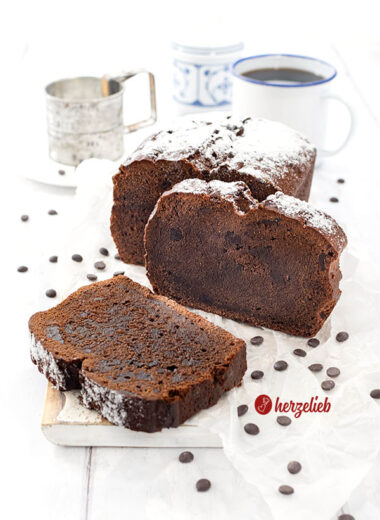 Schokokuchen nach einem Frischkäse-Schokoladenkuchen Rezept von herzelieb. Der Kuchen liegt auf eine weißen Brett und ist angeschnitten. Eine Scheibe lehnt am Kuchenlaib, die andere liegt davor.