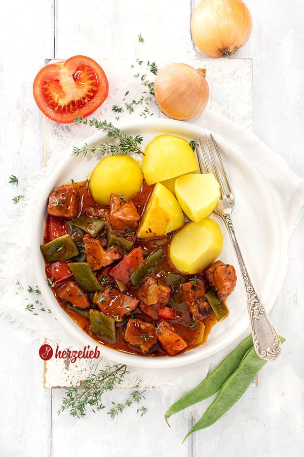 Kartoffeln mit Kasseler Gulasch auf einem Teller angerichtet. Im Gericht sieht man Bohnen, Kasseler Nacken, Tomaten in dunkler Soße 