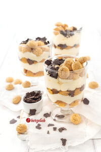 3 Schichtdesserts im Glas nach einem Flensburger Präsidentencreme Rezept von herzelieb. Die Die Gläser stehen versetzt hintereinander und jedes ist dekoriert mit Amarettini und Raspelschokolade. Vor, neben und hinter den Gläsern liegen weitere Plätzchen.