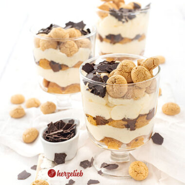 3 Schichtdesserts im Glas nach einem Flensburger Präsidentencreme Rezept von herzelieb. Die Die Gläser stehen versetzt hintereinander und jedes ist dekoriert mit Amarettini und Raspelschokolade. Vor, neben und hinter den Gläsern liegen weitere Plätzchen.