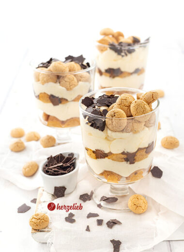 3 Schichtdesserts im Glas nach einem Flensburger Präsidentencreme Rezept von herzelieb. Die Die Gläser stehen versetzt hintereinander und jedes ist dekoriert mit Amarettini und Raspelschokolade. Vor, neben und hinter den Gläsern liegen weitere Plätzchen.