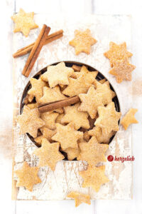 Eine Blechdose mit Plätzchen nach einem Rahmplätzchen Reept von herzelieb. Es sind Sterne, die eine Zimt-Zucker-Kruste haben und die goldbraun gebacken sind. Dekoriert mit Zimtstangen..