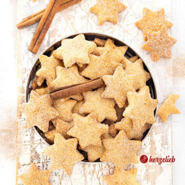 Eine Blechdose mit Plätzchen nach einem Rahmplätzchen Reept von herzelieb. Es sind Sterne, die eine Zimt-Zucker-Kruste haben und die goldbraun gebacken sind. Dekoriert mit Zimtstangen..