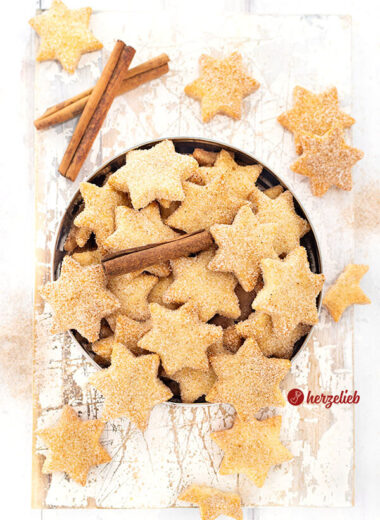 Eine Blechdose mit Plätzchen nach einem Rahmplätzchen Reept von herzelieb. Es sind Sterne, die eine Zimt-Zucker-Kruste haben und die goldbraun gebacken sind. Dekoriert mit Zimtstangen..