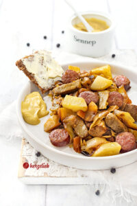 Ein Teller mit Kohleintopf nach einem Sømandskål Rezept aus Dänemark. Im Gericht sieht man Kartoffeln, Kohlwurst, Filtestücke, Weißkohl und Möhren