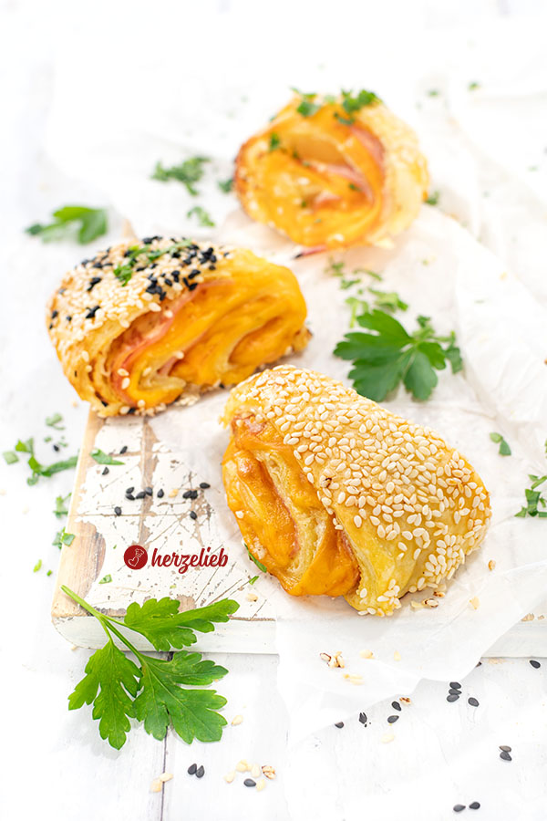 3 herzhaft gefüllte Bätterteigteilchen nach einem Blätterteigschnitten Rezept auf einem weißen Holzbrett. Dekoriert mit Petersilie.