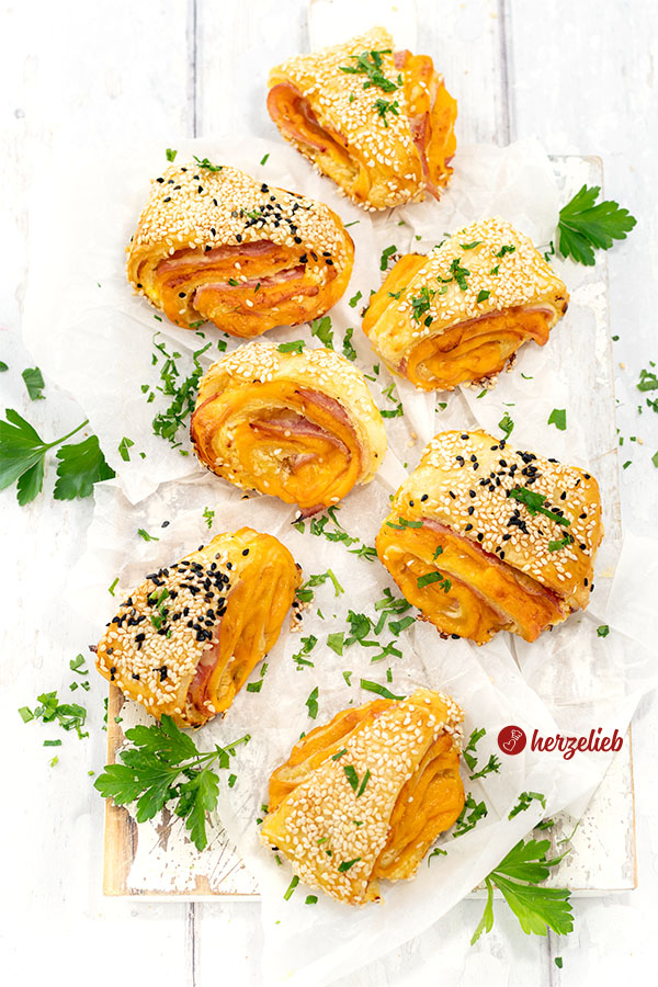Sieben, mit Käse und Schinken gefüllte Blätterteigteilchen nach einem Blätterteigschnitten Rezept von herzelieb. Dekoriert mit Petersilie.