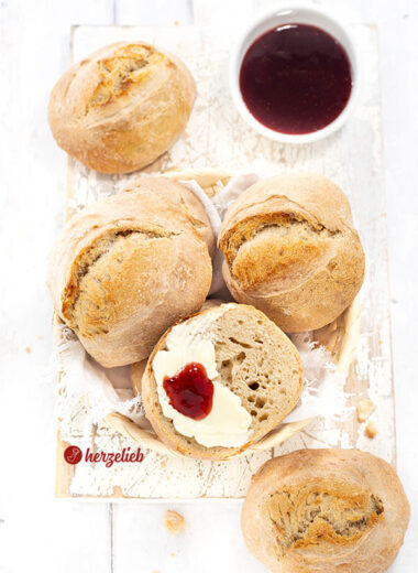 Ein Körbchen mit Brötchen nach einem Ohne-Kneten-Brötchen Rezept von herzelieb. Eine Brötchenhälfte ist bestrichen mit Butter und einem Klecks Marmelade.