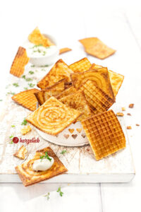 Dünne, knusprige und goldbraune Waffeln nach einem Käsewaffeln Rezept für das Zimtwaffeleisen. Angerichtet in einer kleine, weißes Schale. Im Hintergrund ein Schälchen Dip. Dekoriert mit Kresse.