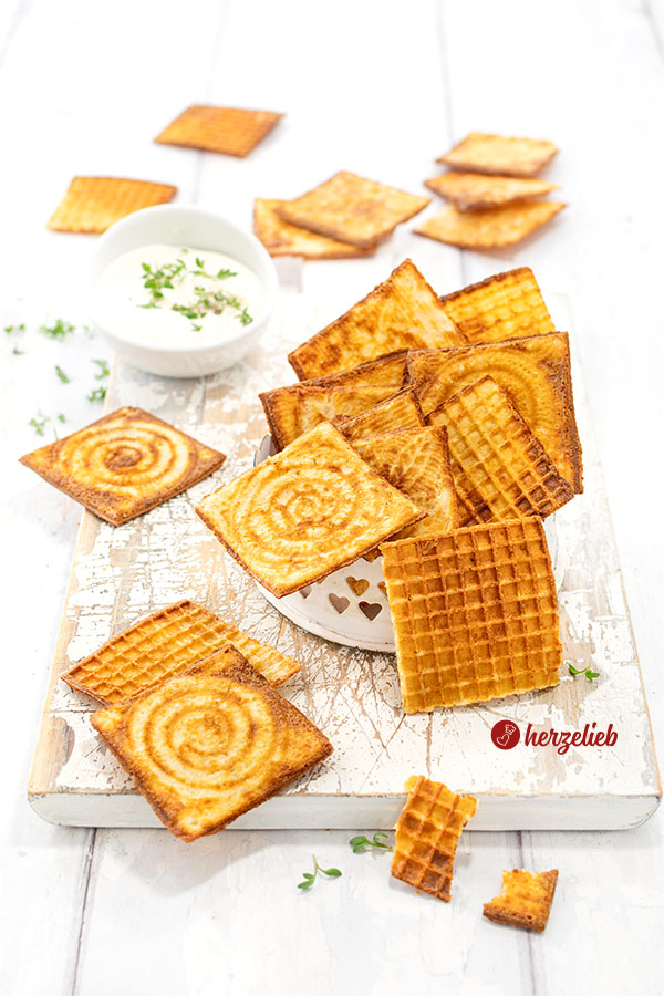 Leckere, knusprige Käsewaffeln. aus dem Zimtwaffeleisen. Angerichtet auf einem weißen Holzbrett, im Hintergrund eine Schale Dip. Dekoriert mit Kresse