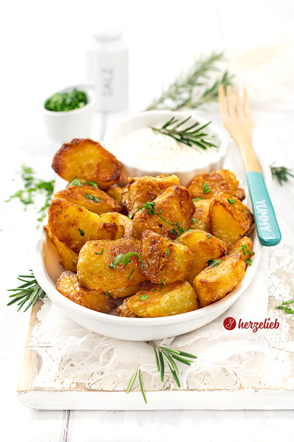 Superknusprige Kartoffeln nach einem Knusperkartoffeln Rezept von herzelieb. Angerichtet auf einer weißen Porzellanschale, zusammen mit einem Schälchen Dip, bestreut mit gehackter Petersilie und dekoriert mit Rosmarin