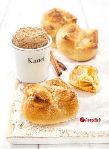 Kronerboller, die weichen Hefebrötchen mit Zimt und Butter auf ein weißen Tuc. Im Hintergrund ein Zimtgefäß, Zimtstangen und weitere Brötchen.