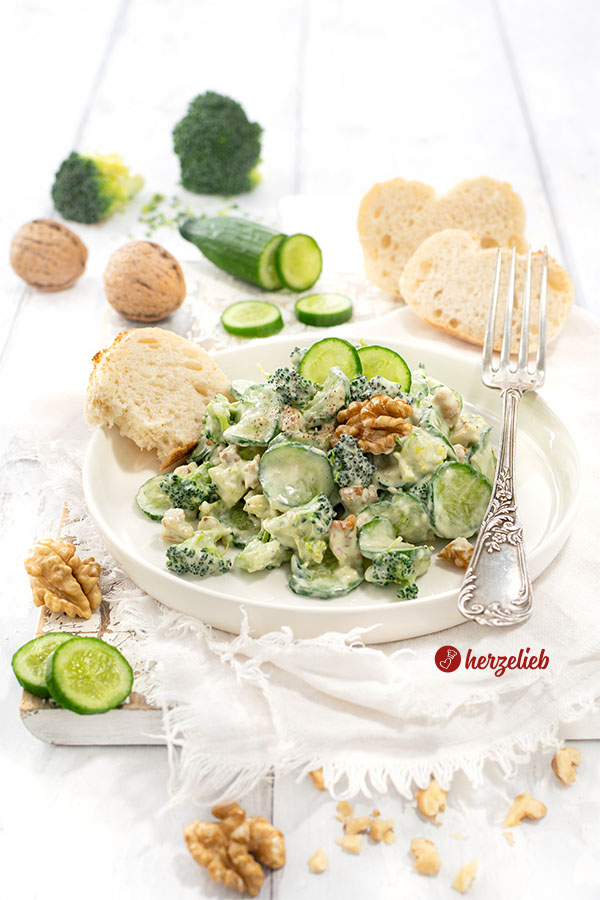Ein Salatteller mit einem cremigen  Gurken-Brokkoli-Salat. Dekoriert mit Walnuss, serviert mit Brot. 