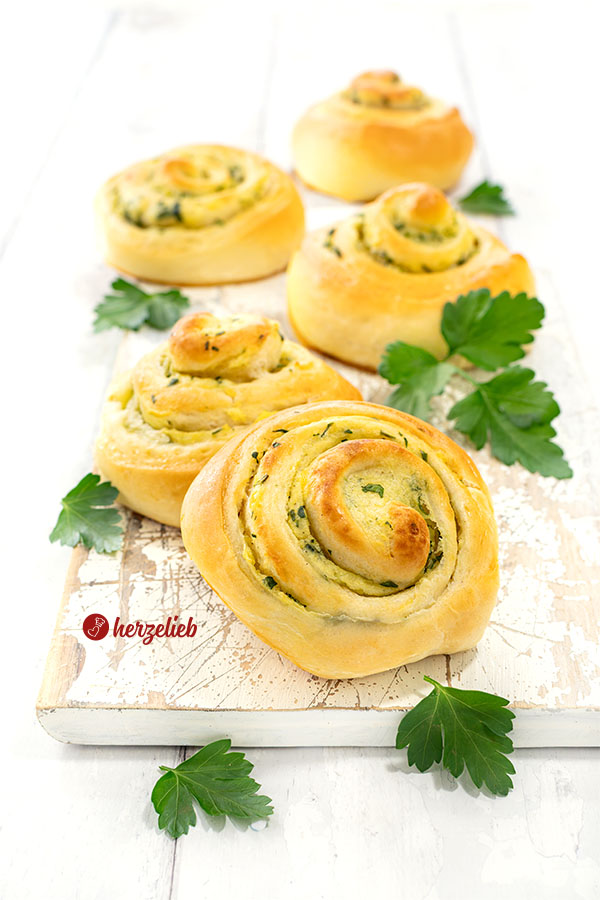 5 herzhafte Hefeschnecken nach einem Kartoffelschnecken Rezept von herzelieb auf einem weißen Brett. Saftig, zartgebräunt, dekoriert mit glatter Petersilie.