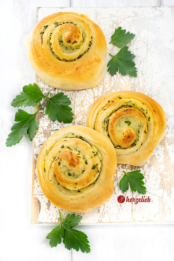 3 saftige und  herzhafte Hefeschnecken nach einem Kartoffelschnecken Rezept von herzelieb auf einem weißen Brett. Zartgebräunt, dekoriert mit glatter Petersilie.
