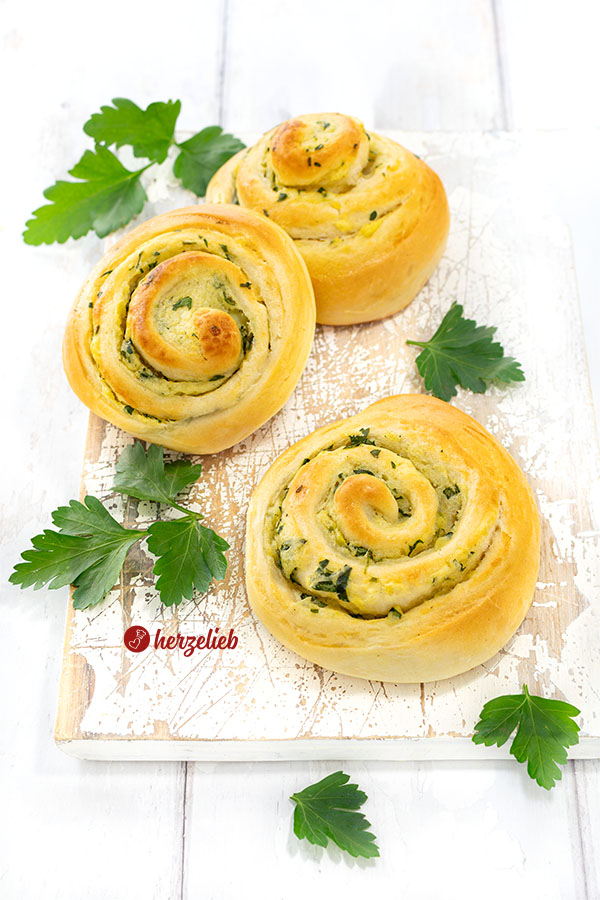 Drei Herzhafte Kartoffelschnecken nach einem Hefeschnecken Rezept von herzelieb auf einem weißen Brett. Zart gebräunt, saftig und, dekoriert mit glatter Petersilie.