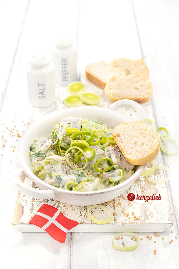 Dänischer Porresild in einer flachen Schale. Der Heringssalat mit Lauch ist angerichtet mit Brot, dekoriert mit Lauchringen und Senfkörnern. I