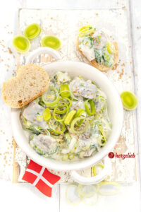 Eine Schale mit Heringssalat mit Lauch einem Porresalat Salat Rezept aus Dänemark. Dekoriert mit Senfkörner und Lauchringen.