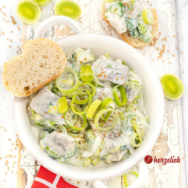 Eine Schale mit Heringssalat mit Lauch einem Porresalat Salat Rezept aus Dänemark. Dekoriert mit Senfkörner und Lauchringen.