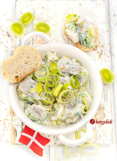 Eine Schale mit Heringssalat mit Lauch einem Porresalat Salat Rezept aus Dänemark. Dekoriert mit Senfkörner und Lauchringen.