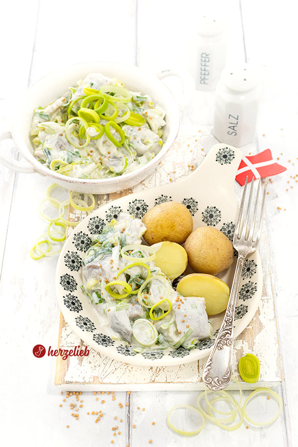 Lauch-Heringssalat nach einem Porresild Rezept aus Dänemark. Angerichtet in einer flachen, hellen Schale mit blauem Dekor. Dekoriert mit Lauch und Senfkörnern