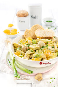 Omas Geflügelsalat mit Mandarinen in einer weißen Schüssel, dekoriert mit Brot. Im Salat außerdem Pilze und Spargel mit Currydressing.