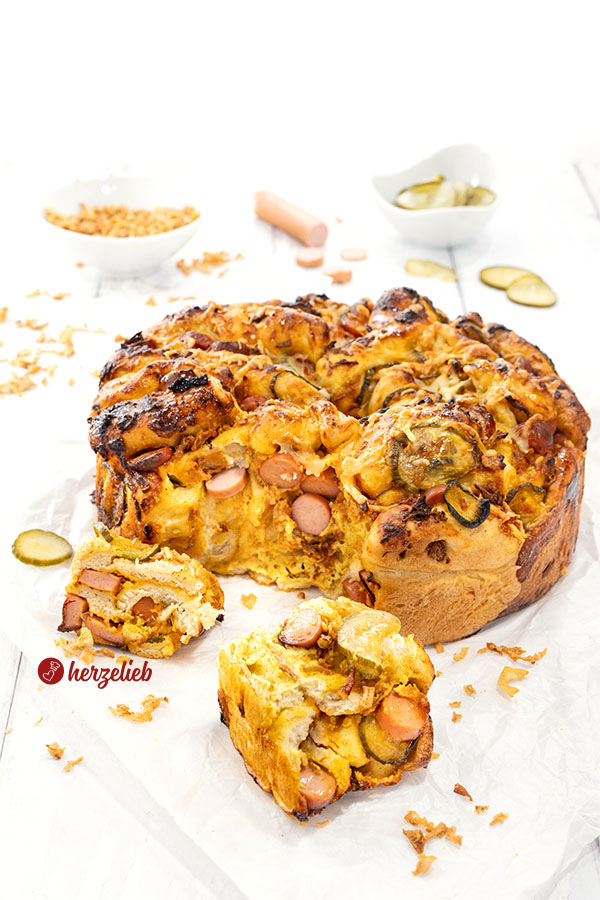 Hotdog-Faltenbrot, goldbraun gebacken auf weißem Backpapier. Vor dem Zupfbrot lieben zwei Stücke davon. 