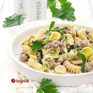 Nahaufnahme der Hack-Lauch-Nudelpfanne mit Käse auf einem weißen Teller mit hohem Rand. Dekoriert mit glatter Petersilie.