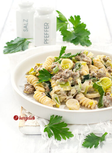 Nahaufnahme der Hack-Lauch-Nudelpfanne mit Käse auf einem weißen Teller mit hohem Rand. Dekoriert mit glatter Petersilie.