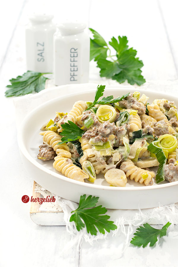 Nahaufnahme der Hack-Lauch-Nudelpfanne mit Käse auf einem weißen Teller mit hohem Rand. Dekoriert mit glatter Petersilie. 