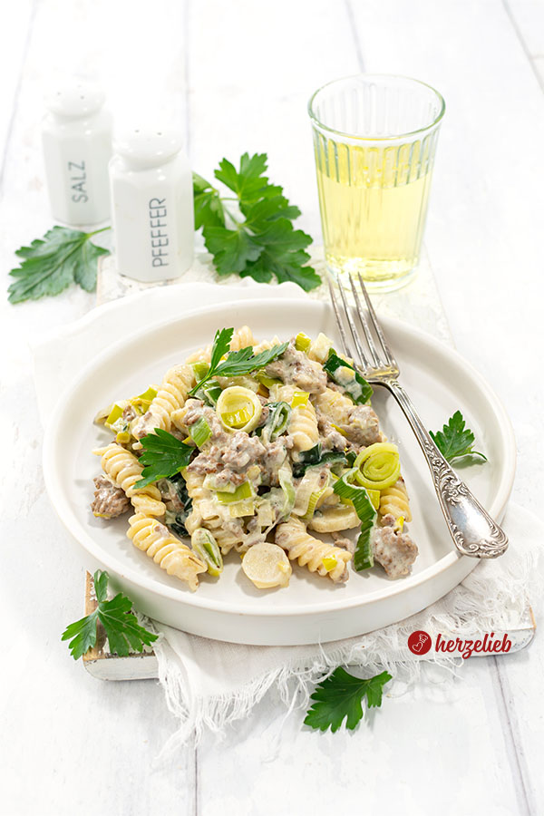 Hack-Lauch-Nudelpfanne auf einem weißen Teller mit hohem Rand. Dekoriert mit glatter Petersilie. Auf dem Tellerrand eine Silbergabel. 