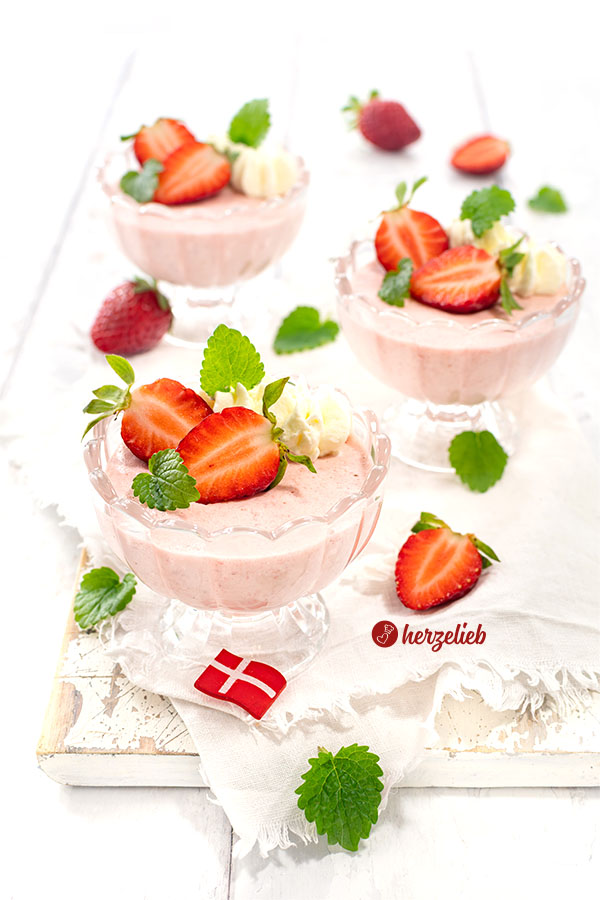 Rosa Jordbærfromage aus Dänemark in 3 Gläsern. Das Erdbeerdessert im Glas ist dekoriert mit Zitronenmelisse und frischen Erdbeeren.