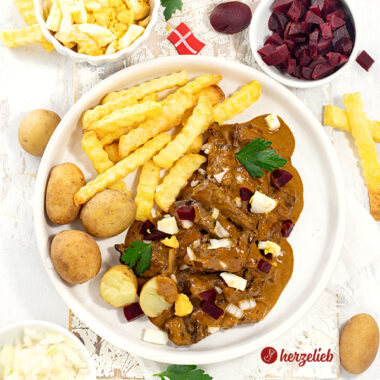 Kong Fiddes Livret mit Pommes und Kartoffeln auf einem Teller angerichtet. Serviert mit Ei, Rote Bete und Zwiebeln. Dekoriert mit Petersilie.