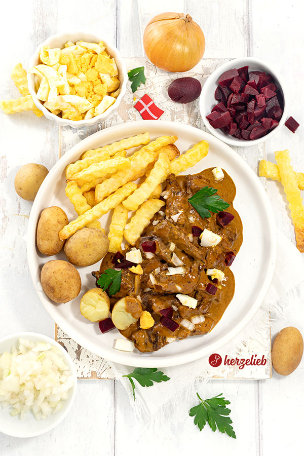 Kong Fiddes Livret mit Pommes und Kartoffeln auf einem Teller angerichtet. Serviert mit Ei, Rote Bete und Zwiebeln. Dekoriert mit Petersilie.