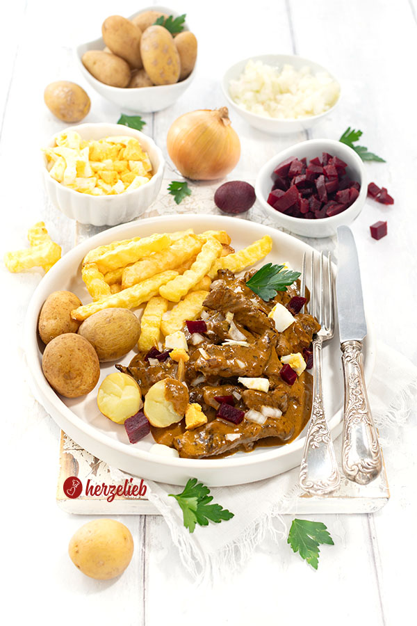 Rindfleisch-Schmorgericht aus Dänemark: Kong Fiddes Livret mit Pommes und Kartoffeln auf einem Teller angerichtet. Mit Ei, Rote Bete und Zwiebeln.