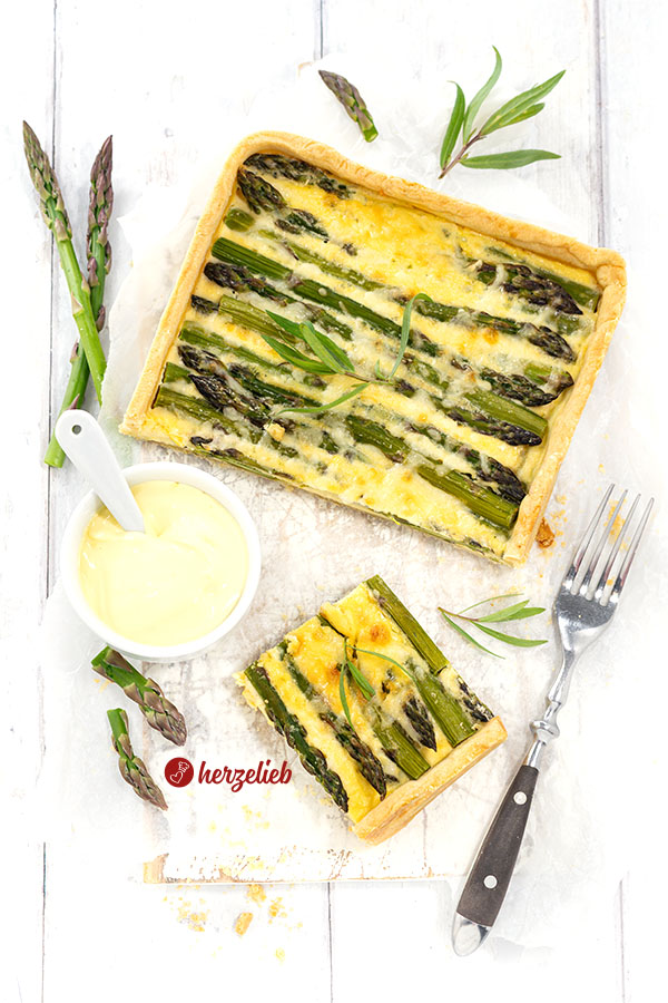 Spargeltarte, angeschnitten. Angerichtet mit Sauce hollandaise. Im Vordergrund ein Stück davon und eine Gabel rechts.