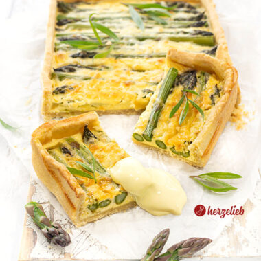 Angeschnittene Spargeltarte mit zwei Stücke die davor lieben. Dekoriert mit Estragon und Spargelspitzen.