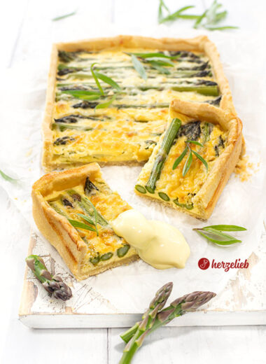 Angeschnittene Spargeltarte mit zwei Stücke die davor lieben. Dekoriert mit Estragon und Spargelspitzen.