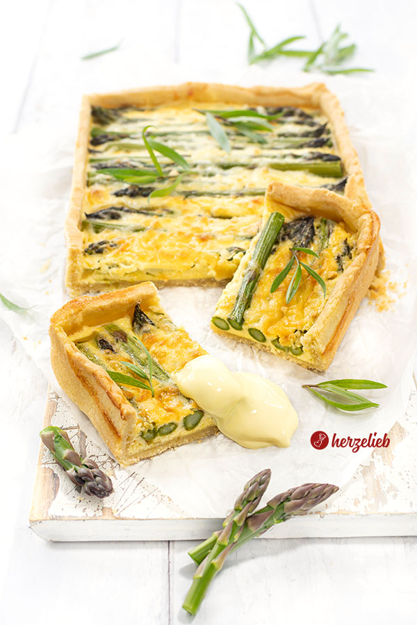 Angeschnittene Spargeltarte mit zwei Stücke die davor lieben. Dekoriert mit Estragon und Spargelspitzen.