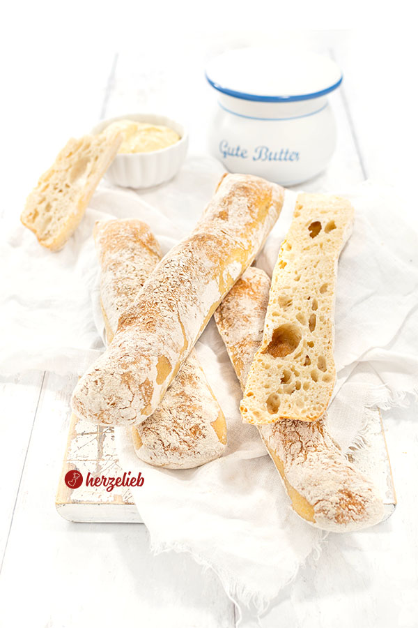 Einige Dinkelstangen mit einem Schälchen Dip. Die Brotstangen liegen übereinander, eine ist aufgeschnitten. 