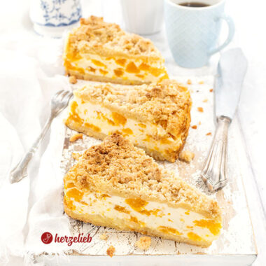 3 Stücke Mandarinen-Schmandkuchen wie von Oma auf einem Holzbrett. Im Vordergrund ein silberner Torenheber. Hinten 2 Kaffeebecher und ein Zuckertopf
