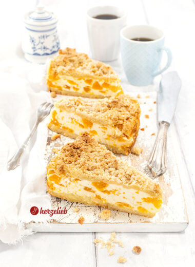 3 Stücke Mandarinen-Schmandkuchen wie von Oma auf einem Holzbrett. Im Vordergrund ein silberner Torenheber. Hinten 2 Kaffeebecher und ein Zuckertopf