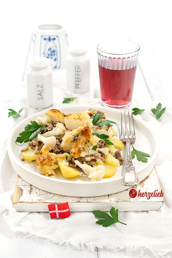 Ein Teller Samsøfad aus Dänemark mit Kartoffeln, Hackfleisch und Blumenkohl. Der Kartoffelauflauf ist dekoriert glatter Petersilie