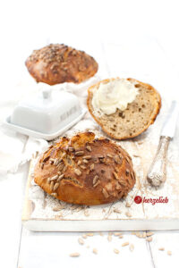 Goldbraun gebackene Sonnenblumenkernbrötchen. Ein Messer und eine Butterdose im Hintergrund.