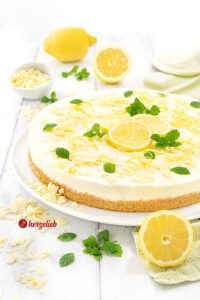Frischer Buttermilch-Zitronenkuchen auf einem Teller. Dekoriert mit Zitronen und weißer Schokolade.
