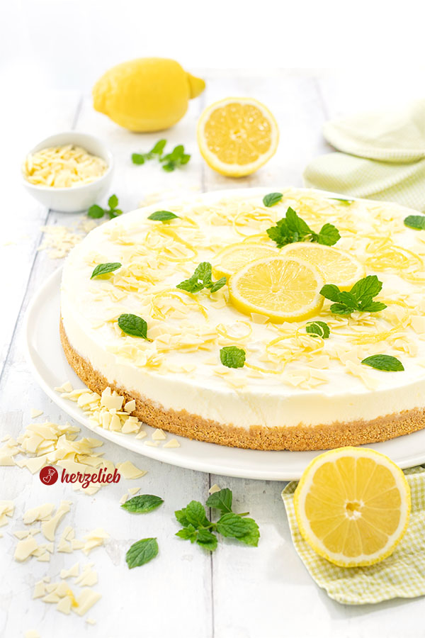 Frischer Buttermilch-Zitronenkuchen auf einem Teller. Dekoriert mit Zitronen und weißer Schokolade.