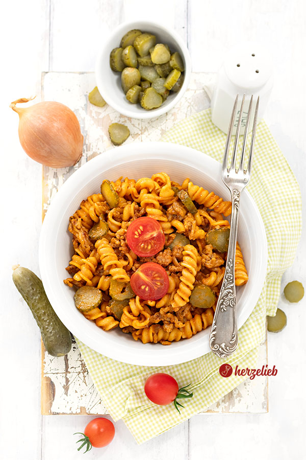 Schnelle Cheeseburger-Pasta in einer Schale. Dekoriert mit Tomate, auf dem Schüsselrand eine Gabel. 
