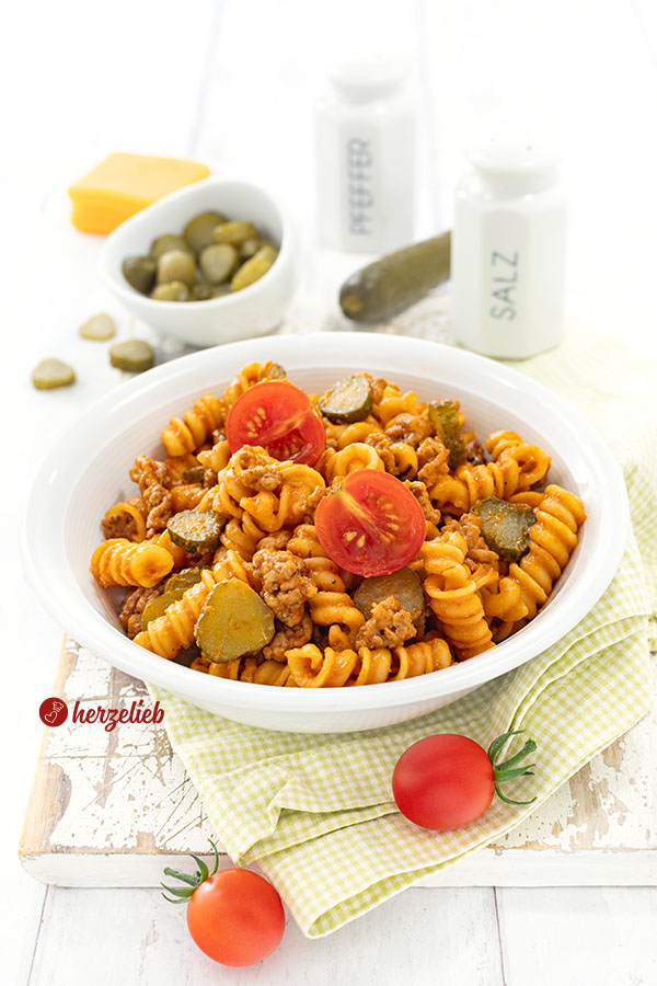 Leckere Cheeseburger-Pasta in einer Schale, die auf einem Brett steht. Im Vordergrund Tomaten.