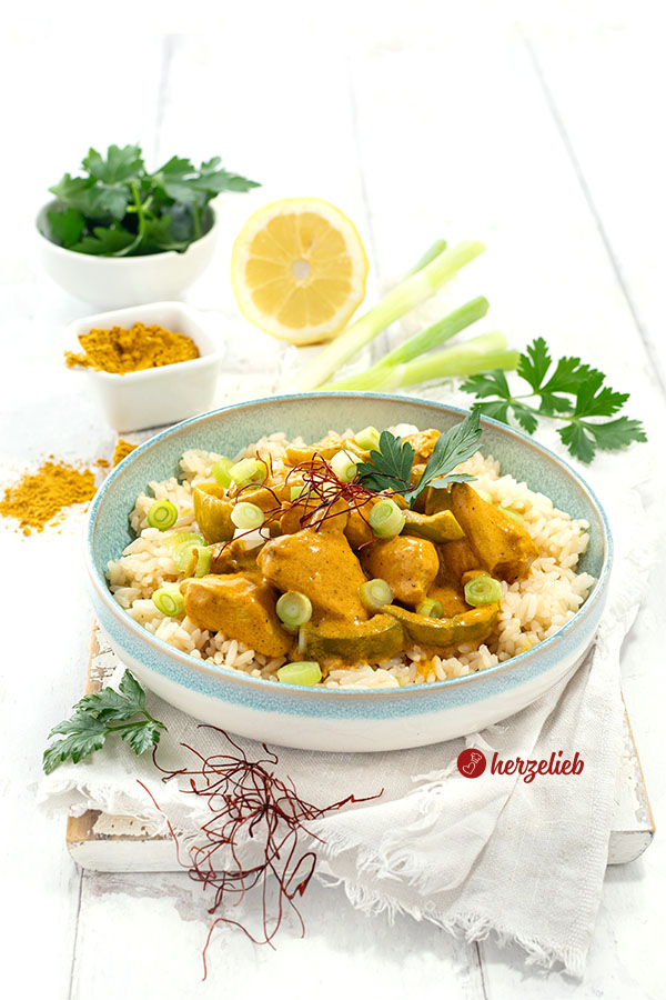 Ein Teller mit einem Geflügelgericht nach einem Curry-Schmand-Hähnchen Rezept von herzelieb. Angerichtet mit Reis, dekoriert mit Chilifäden und Petersilie